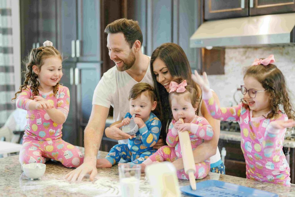 The Riff family of six—parents with four children—gathered together in their modern kitchen, smiling beside a polished stone slab countertop.”