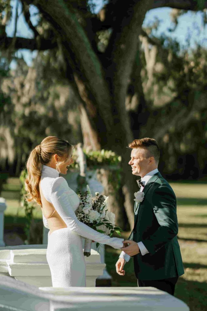 Fraiser in an olive green suit holding his bride’s hand as she stands beside him in a white wedding dress.